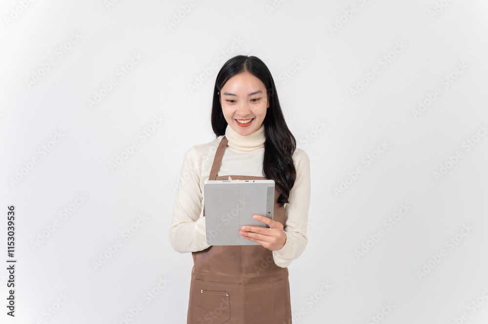 A smiling female waitress or coffee shop staff in a brown apron writes order in her digital tablet. A smiling female waitress or coffee shop staff in a brown apron writes order in her digital tablet.