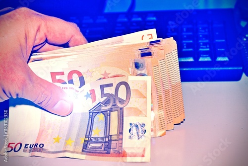 Fotografia Hand holding Euro banknotes with the a computer as a background