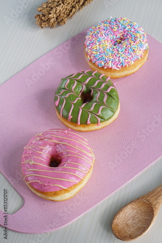 three donuts with strawberry matcha topping and sprinkles, on a pink plastic plate photographed with studio light