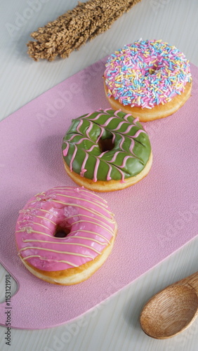 three donuts with strawberry matcha topping and sprinkles, on a pink plastic plate photographed with studio light