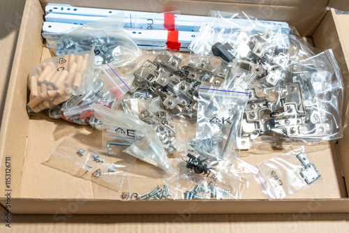 Cardboard box with furniture assembly kit. Screws, wooden dowels, door hinges, bolts, spare parts for furniture assembly.