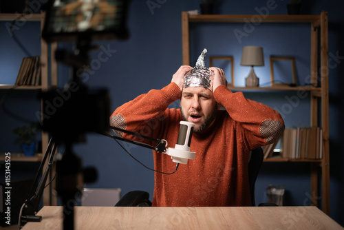 Strange bearded man vlogger in foil hat feeling headache, He recording live stream at home. Fake news conspiracy theory
