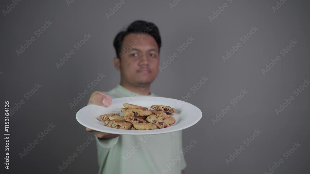 A black-haired Southeast Asian man in front of the camera then lifts a plate full of cookies in front of the camera. A black-haired Southeast Asian man in front of the camera then lifts a plate full of cookies in front of the camera.