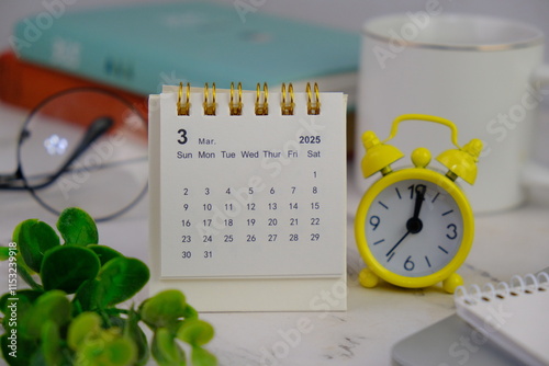 Monthly desk calendar for March 2025 year on wooden table with black alarm clock. photo