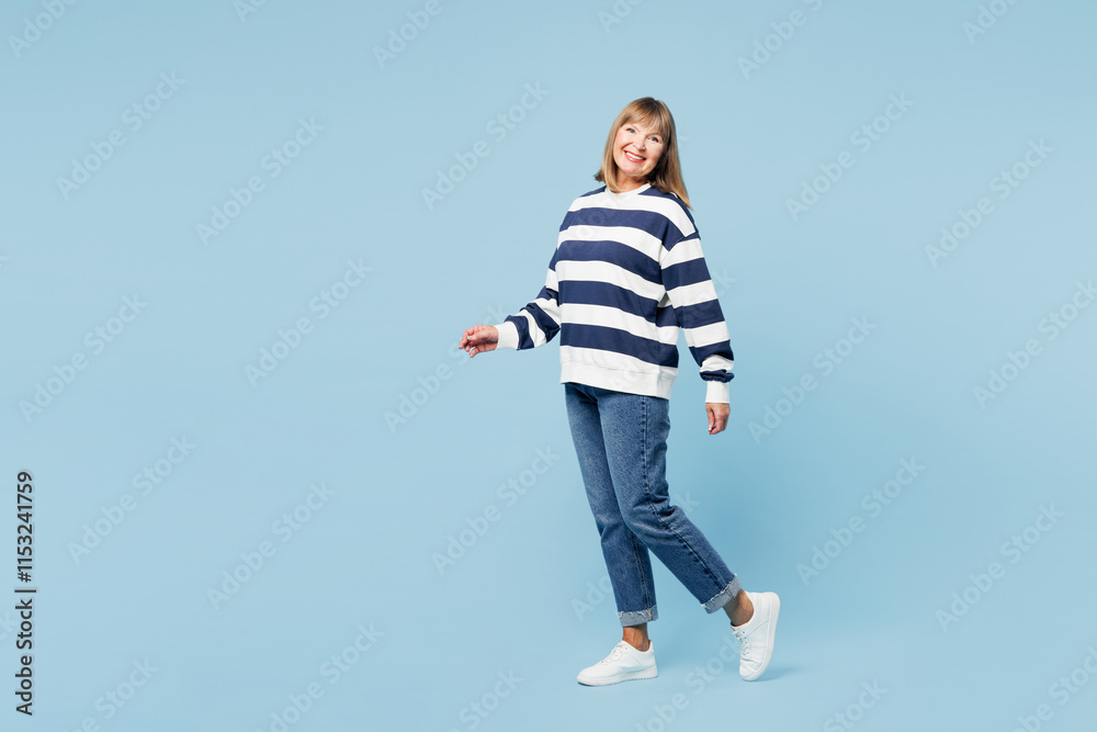 Full body side profile view elderly blonde woman 50s years old wear striped sweatshirt casual clothes walk go look camera isolated on plain pastel light blue cyan background studio. Lifestyle concept. Full body side profile view elderly blonde woman 50s years old wear striped sweatshirt casual clothes walk go look camera isolated on plain pastel light blue cyan background studio. Lifestyle concept.