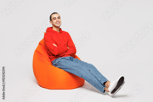 Full body young smiling happy cheerful middle eastern man he wear red hoody casual clothes sit in bag chair looking camera isolated on plain solid white background studio portrait. Lifestyle concept.