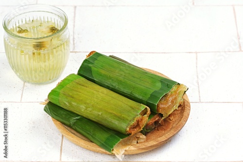 Traditional Indonesian snack Serabi Solo wrapped in banana leaves, served on a wooden plate with a glass of refreshing herbal drink.Perfect for food themes, culture, and traditional cuisine photograpy photo