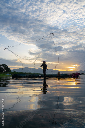 Fisherman casting his net at sunrise. Silhouette Asian fisherman on wooden boat casting a net in the Lake. Vietnamese Fisherman throwing net.