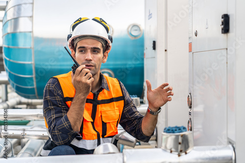 Male technical foreman in safety uniform inspects maintenance work talking on radio call with colleague with to look at plumbing and electrical systems on the roof of a building