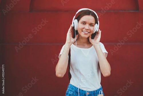 Half length portrait of smiling female meloman enjoying new playlist via headphones, cheerful woman listening radio broadcasting songs outdoors using modern stereo equipment outdoors on leisure photo