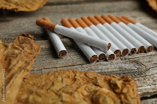 Dried tobacco leaves and cigarettes on wooden table, closeup