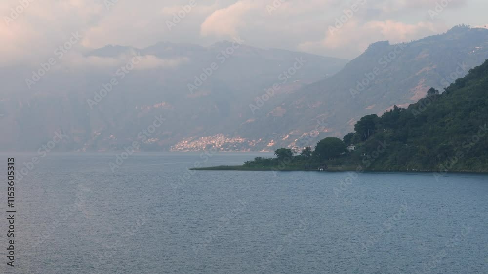 Panoramic view of Lago Atitlan surrounded by forested mountains with a hazy sunset sky Panoramic view of Lago Atitlan surrounded by forested mountains with a hazy sunset sky