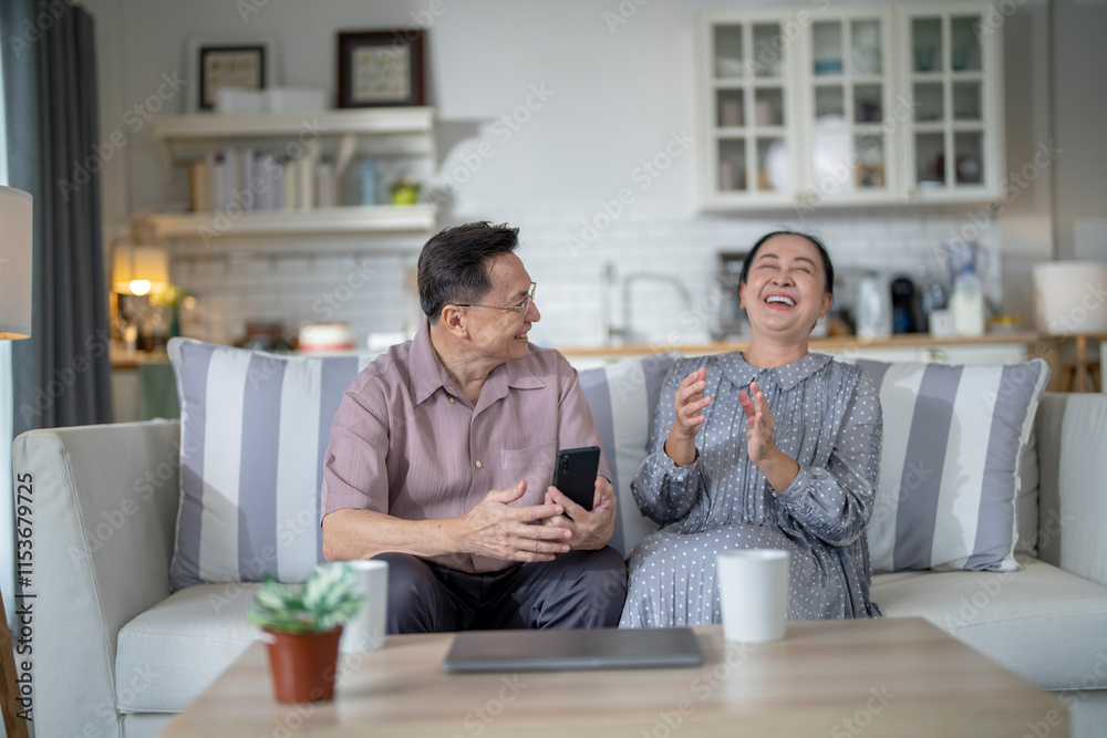 An elderly couple sits together in their cozy living room, smiling and enjoying a moment as they look at something on a smartphone. Their warmth and affection capture a peaceful home atmosphere. An elderly couple sits together in their cozy living room, smiling and enjoying a moment as they look at something on a smartphone. Their warmth and affection capture a peaceful home atmosphere.