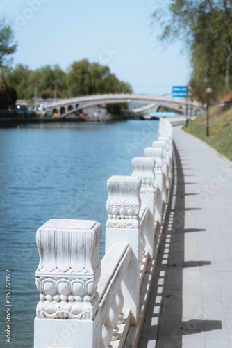 White stone railing along a riverside walkway with a bridge in the background photo