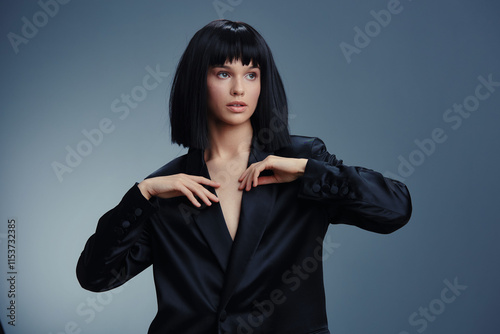 Woman in black suit, hands on chest and hips, posing against gray background, exuding confidence and power photo