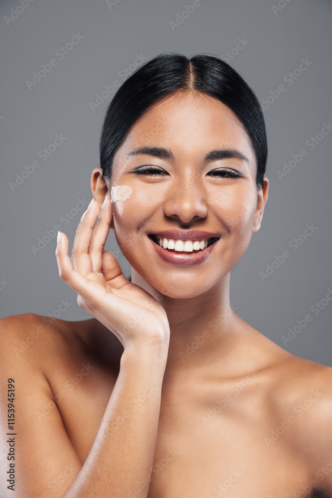 Beautiful woman posing at camera while putting cream on her face on grey isolated background Beautiful woman posing at camera while putting cream on her face on grey isolated background