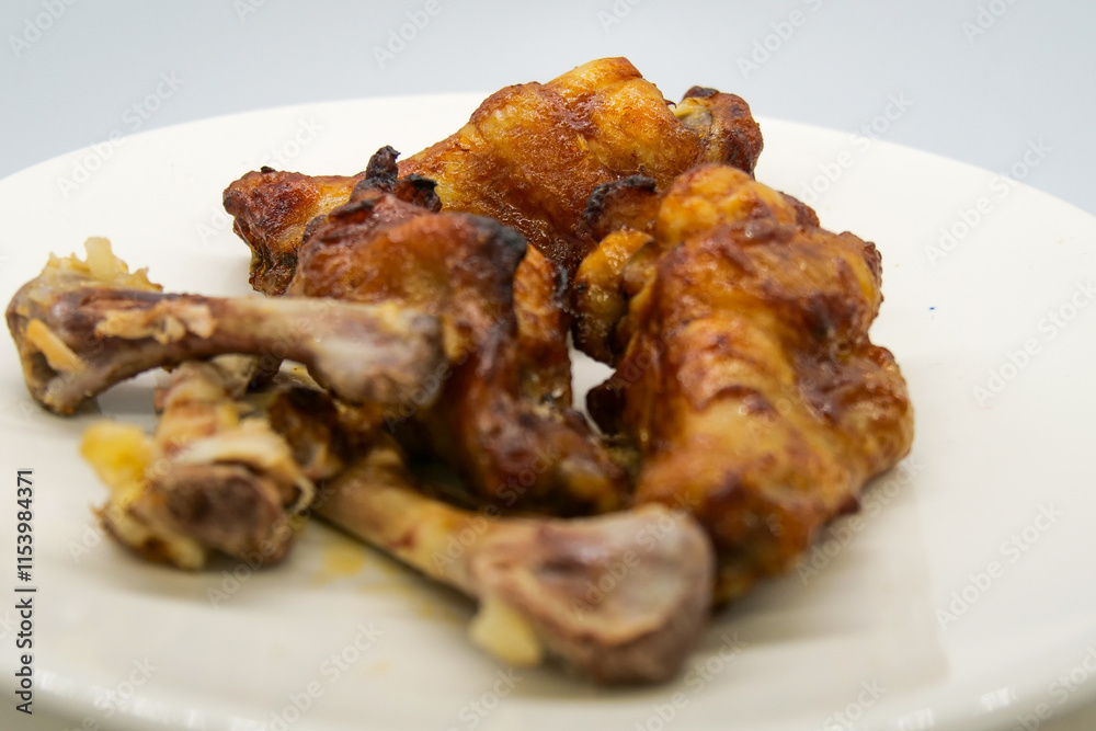 White plate with small brown basted and cooked chickenwings and some chicken bones of wings that has been eaten. White plate with small brown basted and cooked chickenwings and some chicken bones of wings that has been eaten.