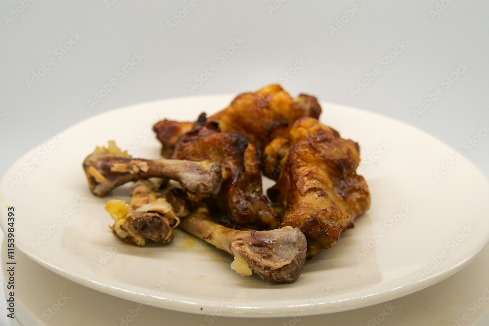 White plate with small brown basted and cooked chickenwings and some chicken bones of wings that has been eaten. White plate with small brown basted and cooked chickenwings and some chicken bones of wings that has been eaten.