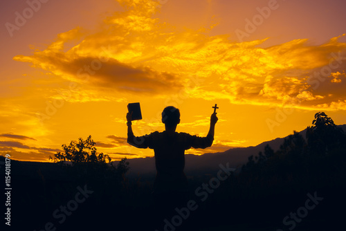 man standing praying and holding christian cross and bible for worshipping God at sunset background. christian silhouette concept.
