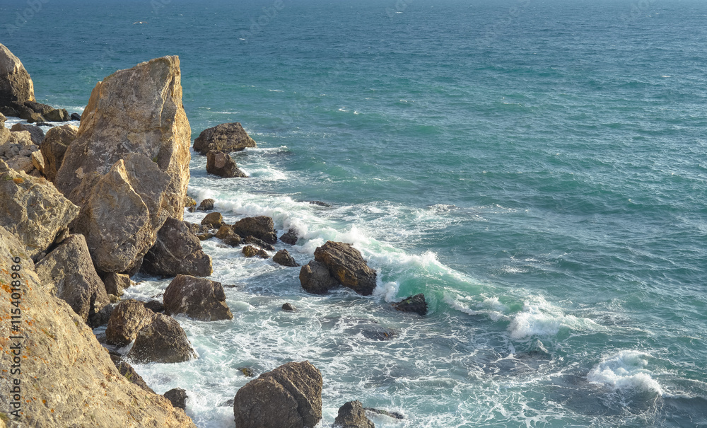 Waves of the Black Sea crash on a rocky shore on a sunny day in Crimea.