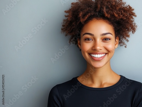 A cheerful young woman with curly hair displays a joyful smile while standing against a light gray backdrop