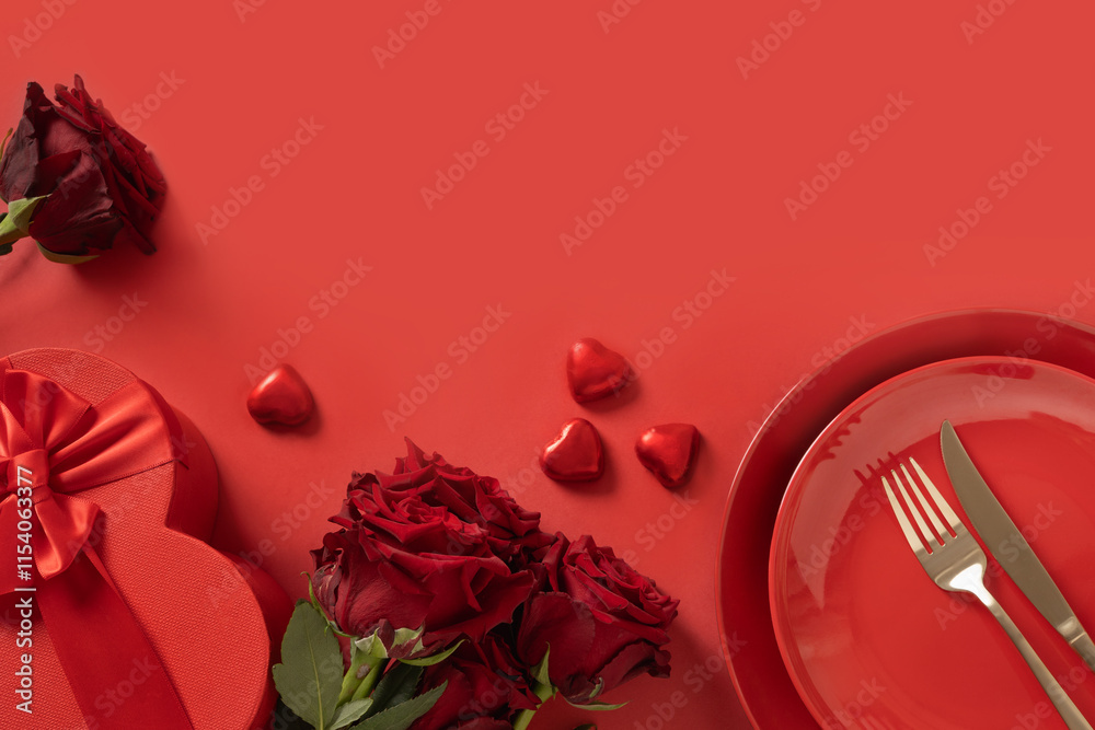 Valentine's day. Romantic table setting with white plate, red chocolate sweets, romantic gift and red roses on red background. Catering. View from above. Copy space.