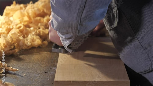 A carpenter plans a board with a hand plane. The sound of shavings is heard