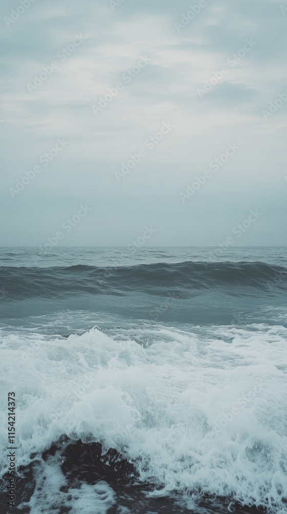 Fototapeta premium Ocean waves crashing on the shore under a cloudy sky