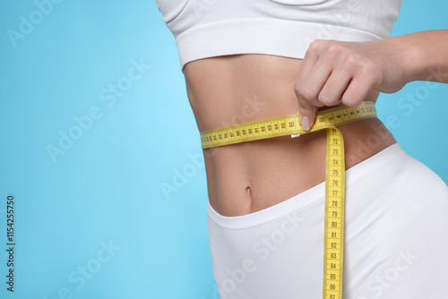 Weight loss. Woman measuring her slim waist with tape on light blue background, closeup. Space for text