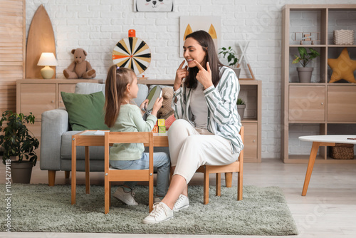 Female speech therapist and little girl with mirror pronouncing letter in office photo