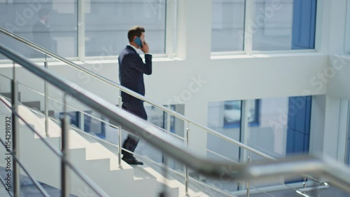 Bearded employee talking cellphone descending office stairs. Confident man 