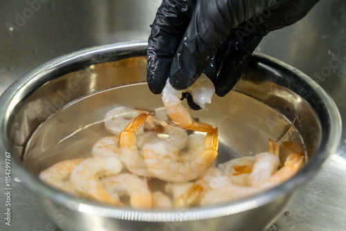 Fotografija cleaned shrimp held by hand in black gloves over stainless steel bowl filled wit
