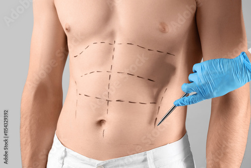 Female plastic surgeon marking man's abdomen on grey background, closeup