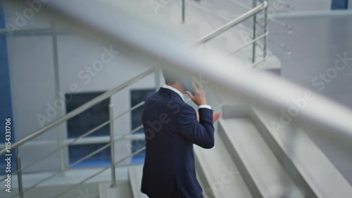 Businessman talking cellphone climbing office stairs. Corporate manager calling