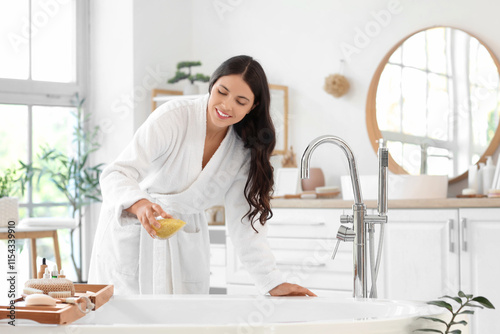Beautiful young happy woman adding sea salt in bathtub at home