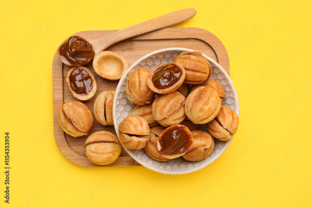 Bowl and wooden board of sweet walnut shaped cookies with boiled condensed milk on yellow background Bowl and wooden board of sweet walnut shaped cookies with boiled condensed milk on yellow background