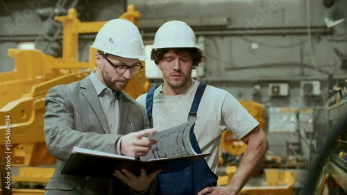 Wallpaper Mural Professional engineer in hard hat and formal suit examining machinery and discussing technical drawings with mechanic in industrial factory Torontodigital.ca