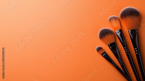 A collection of four makeup brushes against an orange background, showcasing different sizes and softness for various cosmetic applications in beauty routines.