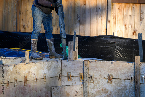 Construction worker walking on wood cement form panels for foundation walls guiding concrete boom pump truck pipe into forms, winter house building project job site
 photo