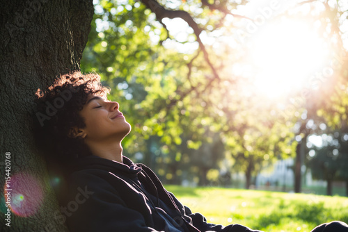 Fototapeta Naklejka Na Ścianę i Meble -  Young african teen relaxing by tree in sunny park