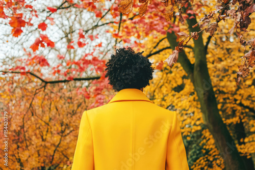 Young african adult male in yellow coat walking through colorful autumn forest photo