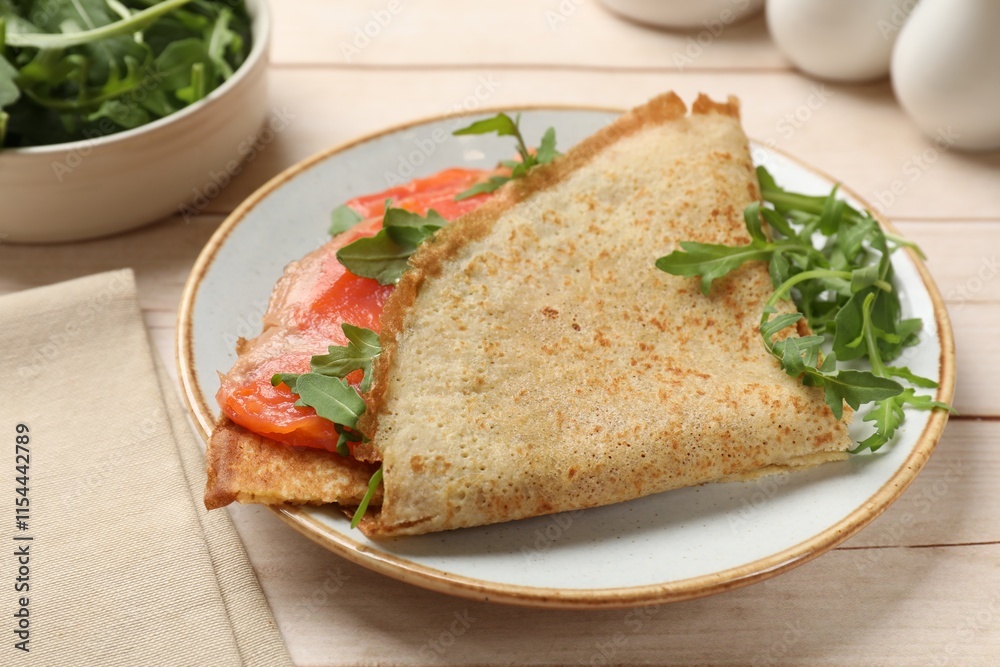 Delicious crepes with salmon and arugula on white wooden table, closeup Delicious crepes with salmon and arugula on white wooden table, closeup