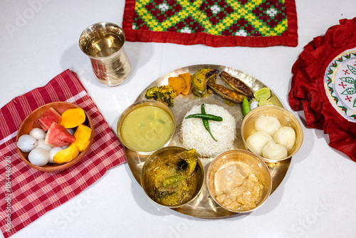 A festive or ceremonial Bengali meal served on a brass thali. Steamed white rice, dal, sorshe ilish or hilsa fish in mustard sauce, rosogolla, clay bowl containing fruit (watermelon, mango, lychee) photo