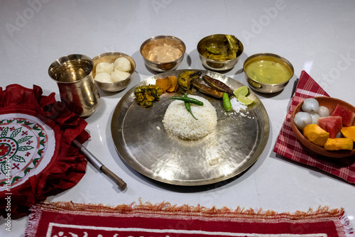 A festive or ceremonial Bengali meal served on a brass thali. Steamed white rice, dal, sorshe ilish or hilsa fish in mustard sauce, rosogolla, clay bowl containing fruit (watermelon, mango, lychee) photo