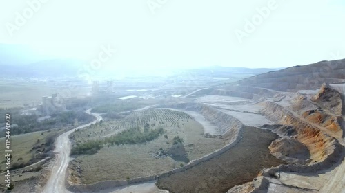 Aerial view of a large open pit cement mine, showing exposed layers, roads and machinery, highlighting the impacts of resource extraction at dusk