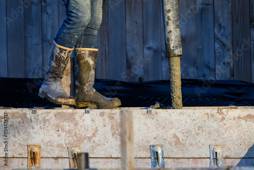 Construction worker walking on wood cement form panels for foundation walls guiding concrete boom pump truck pipe into forms, winter house building project job site
 photo