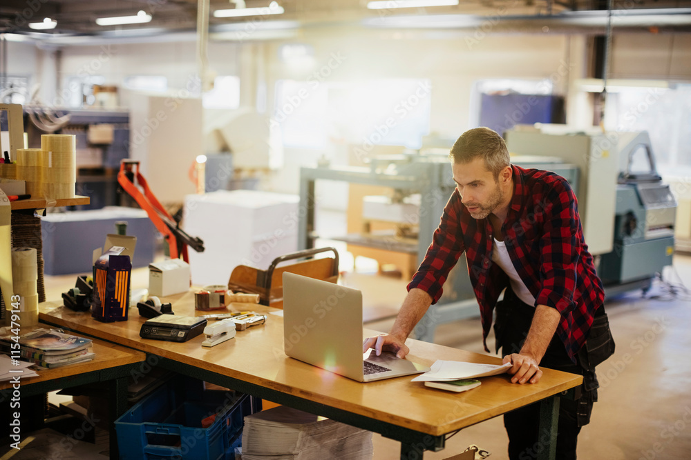 Male factory worker using laptop in industrial printing office Male factory worker using laptop in industrial printing office