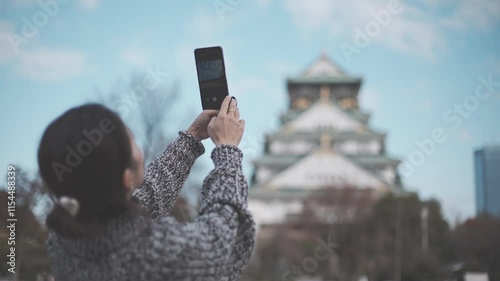 スマホで大阪城を撮る女性旅行者の後ろ姿