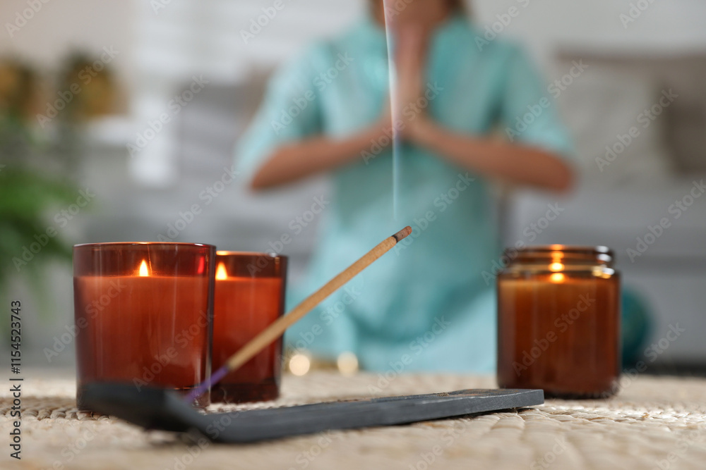 Incense stick smoldering in holder and burning candles on wicker mat indoors, selective focus Incense stick smoldering in holder and burning candles on wicker mat indoors, selective focus