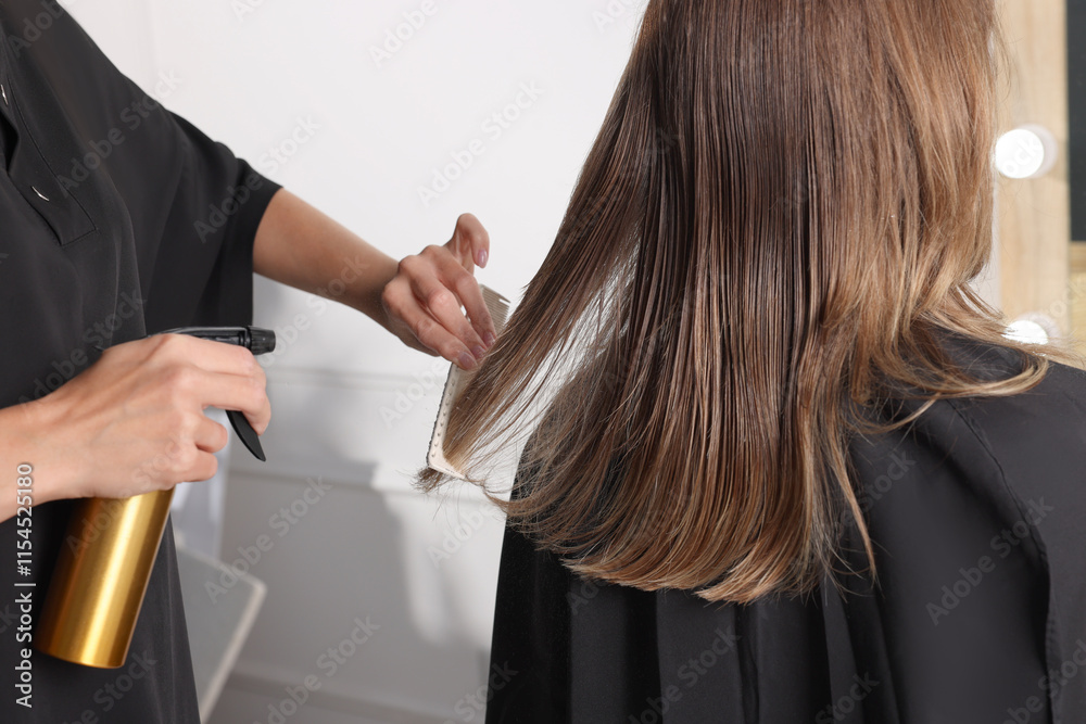 Fototapeta premium Hairdresser using spray while making stylish haircut in salon, closeup